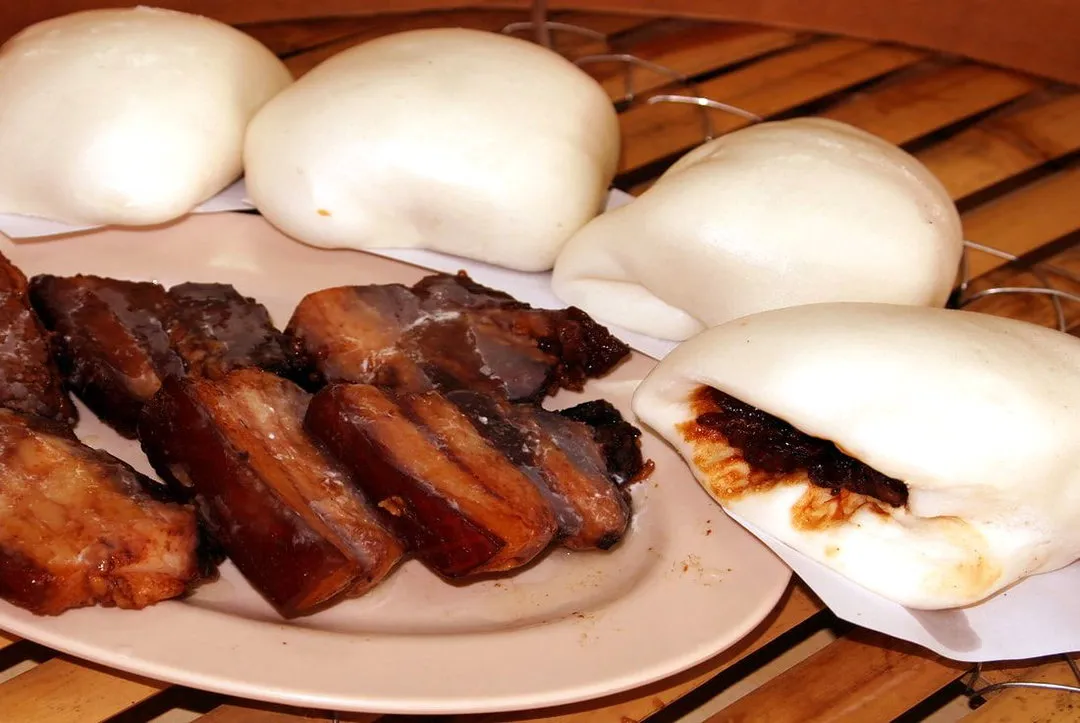 Slices of braised pork belly beside a folded bun
