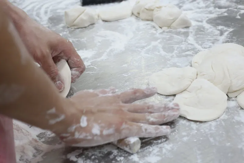 Hands shaping pau dough on a floured steel table
