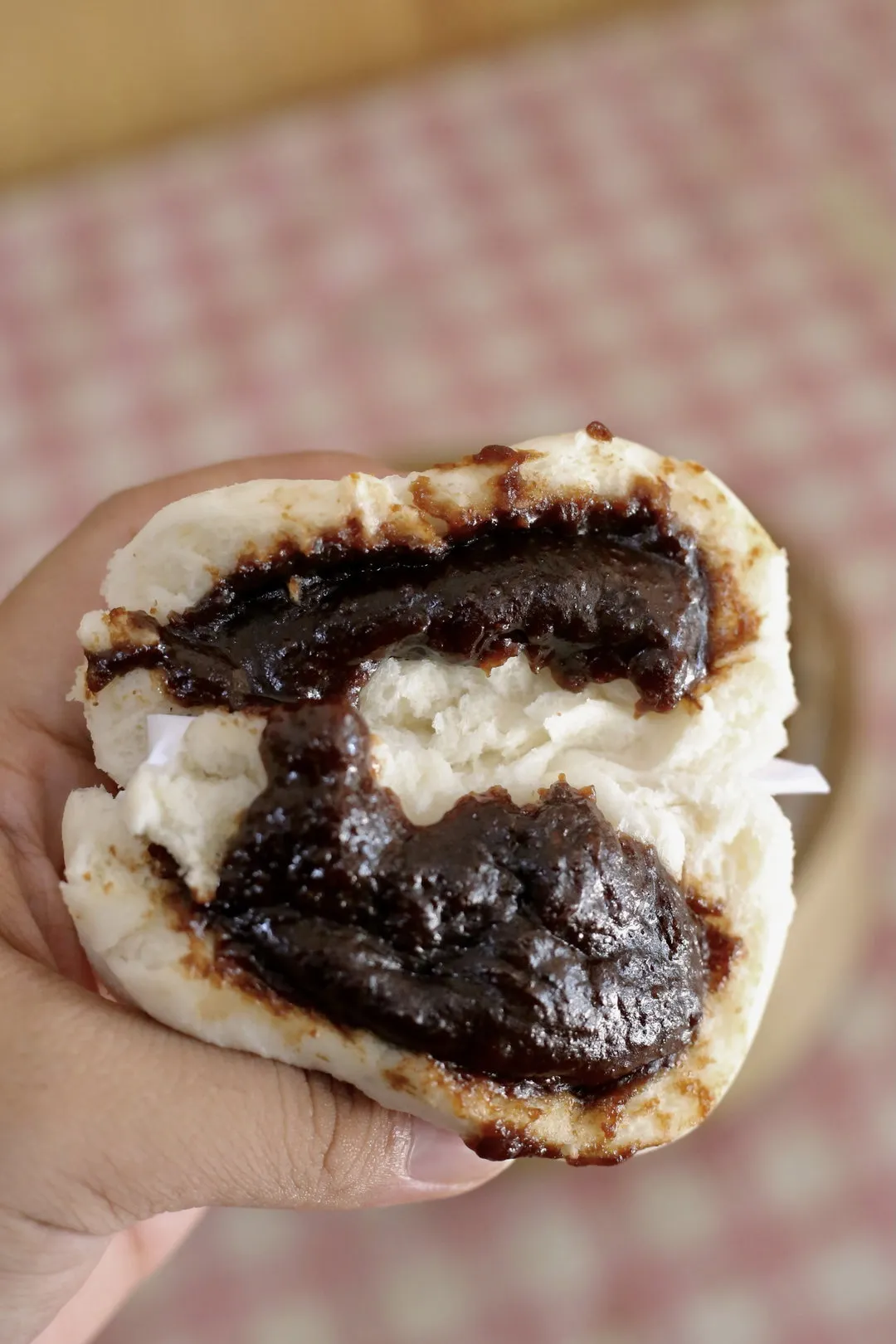 A hand holding a red bean pau torn open to show dark bean paste