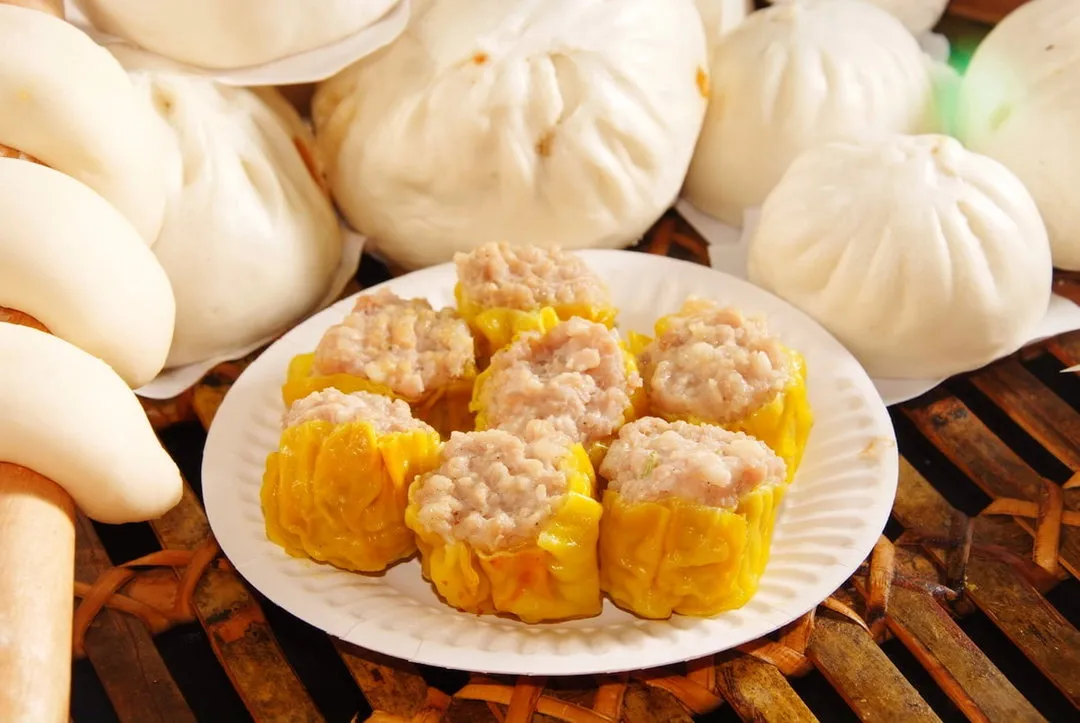 A plate of siew mai in front of a basket of pau