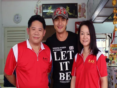 Three people at the shop: a man and a woman in red polos, and a man in a black Let It Be shirt and cap