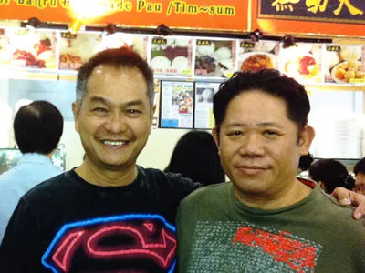 Two men smiling in front of a pau stall